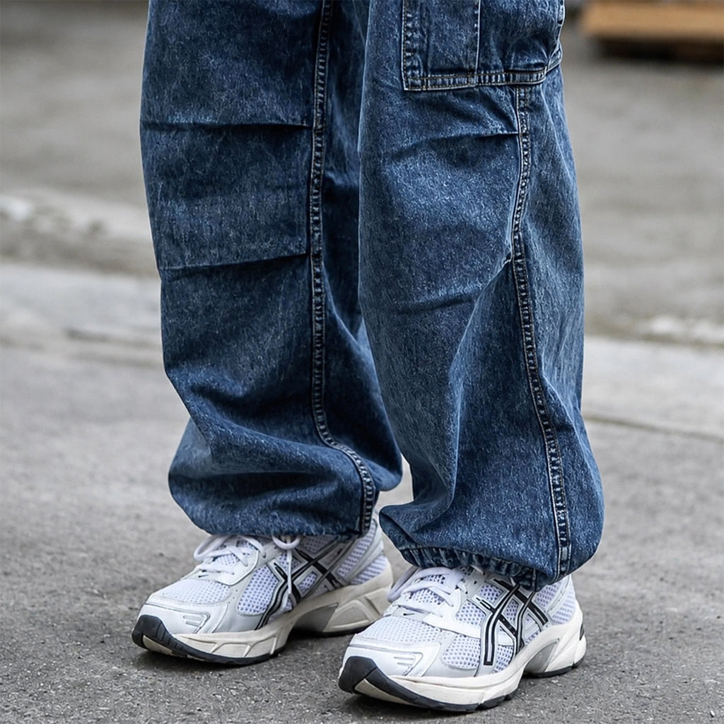 Model wearing white and silver ASICS sneakers with loose-fitting dark blue cargo jeans on a city street.