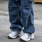 Model wearing white and silver ASICS sneakers with loose-fitting dark blue cargo jeans on a city street.